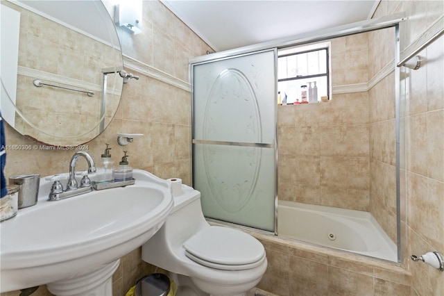 full bathroom with tile walls, toilet, bath / shower combo with glass door, and sink