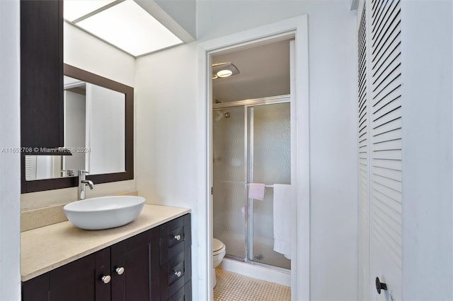 bathroom featuring a shower with door, vanity, toilet, and tile patterned flooring