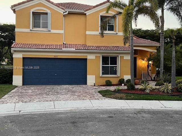 mediterranean / spanish-style home with decorative driveway, a tiled roof, an attached garage, and stucco siding