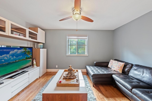 living area featuring a ceiling fan, baseboards, and light wood finished floors