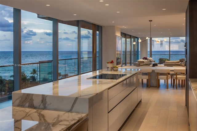 kitchen with light stone countertops, expansive windows, black electric stovetop, a large island, and a water view