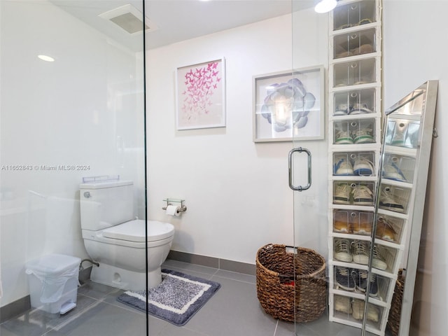 bathroom featuring toilet, a shower with door, and tile patterned floors