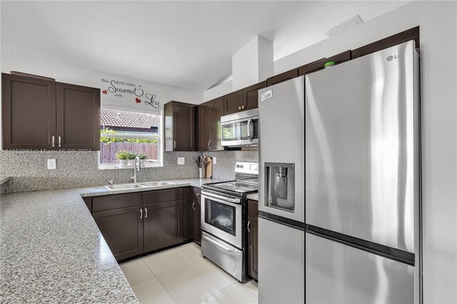 kitchen featuring backsplash, vaulted ceiling, appliances with stainless steel finishes, light stone counters, and sink