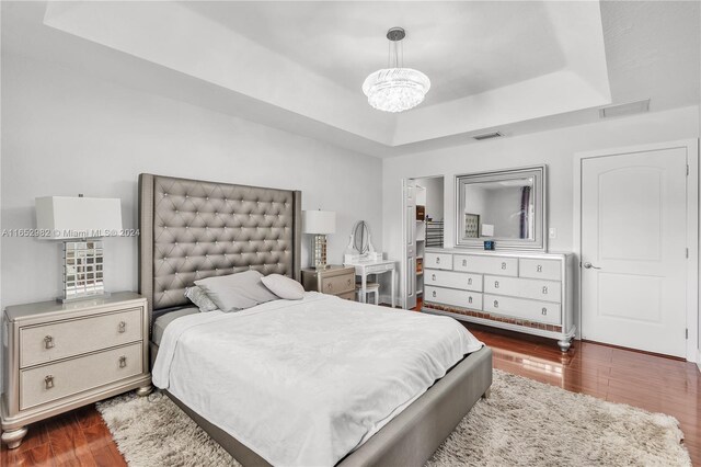 bedroom with a tray ceiling, an inviting chandelier, and dark hardwood / wood-style floors