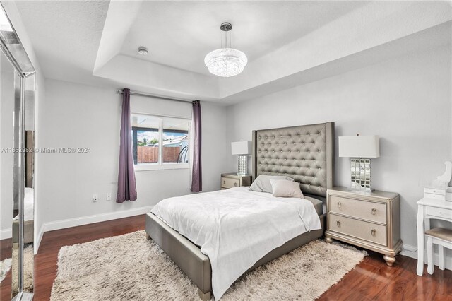 bedroom with dark hardwood / wood-style floors, a raised ceiling, and a notable chandelier