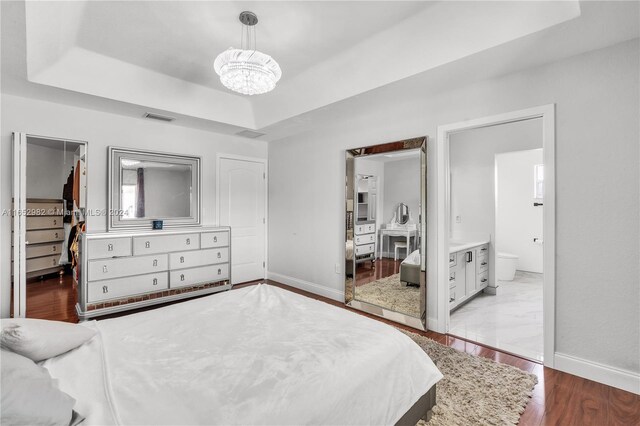 bedroom with ensuite bathroom, light wood-type flooring, a walk in closet, a tray ceiling, and a closet