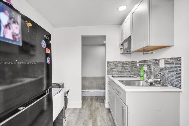 kitchen featuring light hardwood / wood-style flooring, white cabinetry, sink, black appliances, and tasteful backsplash