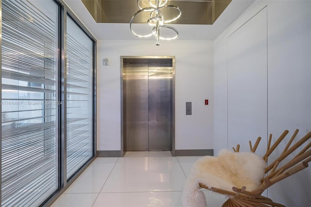 hall featuring light tile patterned floors, a notable chandelier, and elevator