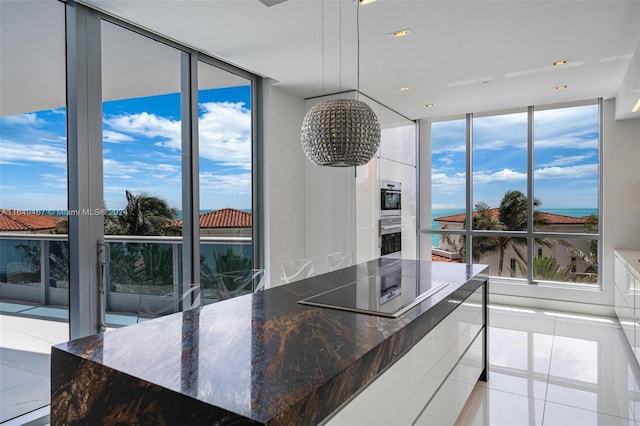 kitchen featuring floor to ceiling windows, dark stone countertops, black electric stovetop, and light tile patterned flooring