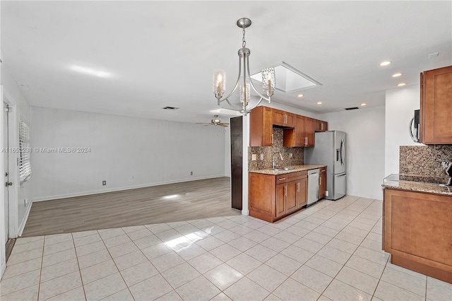 kitchen with light stone counters, ceiling fan with notable chandelier, stainless steel appliances, light wood-type flooring, and sink