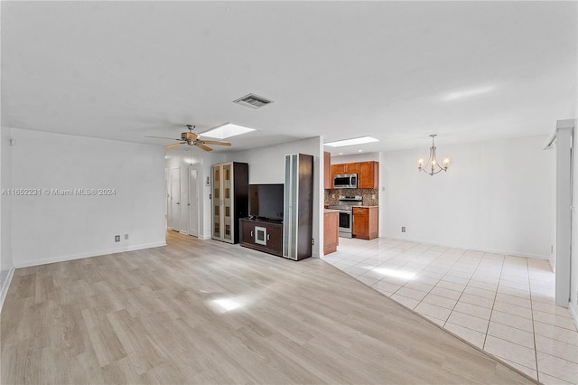 unfurnished living room featuring a skylight, ceiling fan with notable chandelier, and light wood-type flooring