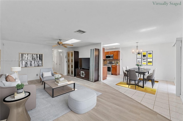 living room with ceiling fan with notable chandelier, light hardwood / wood-style flooring, and a skylight