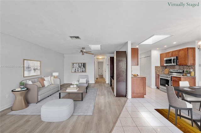 living room with light hardwood / wood-style flooring, ceiling fan, and a skylight