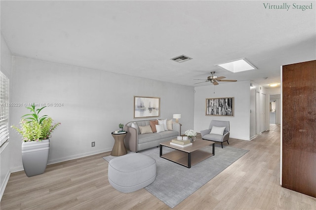 living room featuring ceiling fan, a skylight, and light wood-type flooring