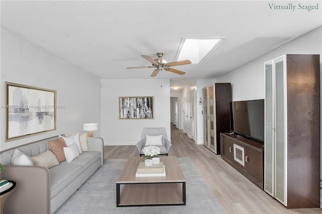 living room with light hardwood / wood-style floors, ceiling fan, and a skylight