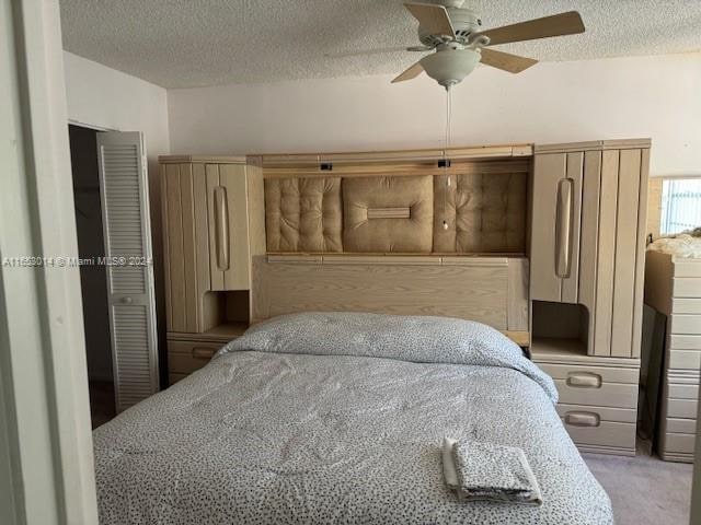 carpeted bedroom featuring ceiling fan and a textured ceiling