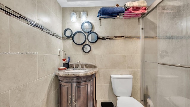 bathroom featuring tile walls, toilet, a shower with door, and vanity