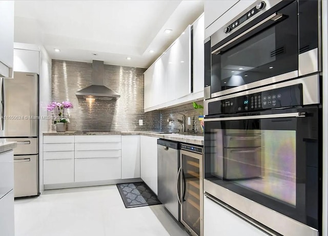 kitchen with white cabinetry, beverage cooler, wall chimney range hood, decorative backsplash, and appliances with stainless steel finishes