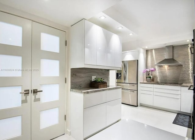 kitchen with decorative backsplash, stainless steel fridge, black electric cooktop, wall chimney range hood, and white cabinetry