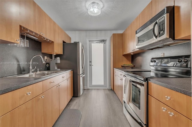 kitchen with light wood-type flooring, stainless steel appliances, sink, and decorative backsplash