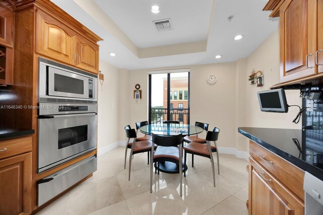 kitchen featuring light tile patterned floors, stainless steel appliances, a raised ceiling, and dark stone counters