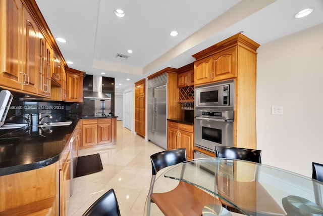 kitchen with light tile patterned floors, sink, wall chimney range hood, built in appliances, and decorative backsplash