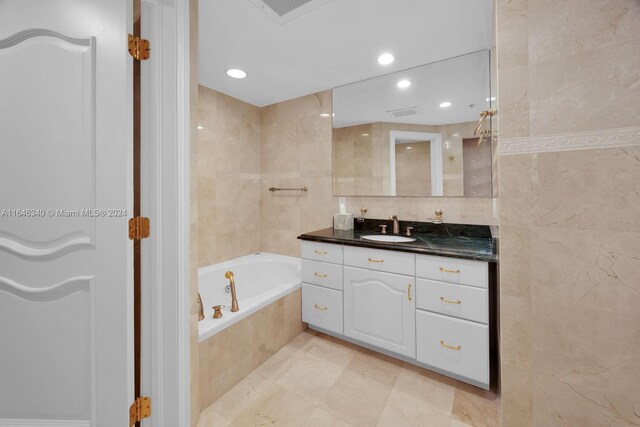 bathroom with tile walls, tiled tub, and vanity