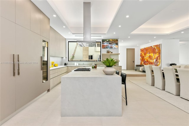 kitchen with a kitchen breakfast bar, stainless steel gas stovetop, light brown cabinetry, a kitchen island, and a tray ceiling