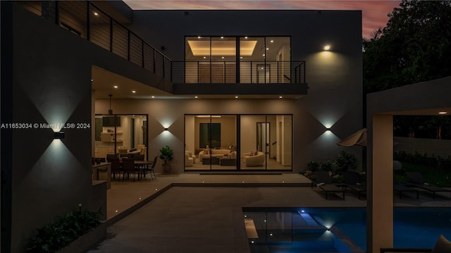 back house at dusk with a balcony and a patio area