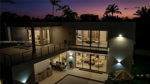 back house at dusk with a balcony and a patio area