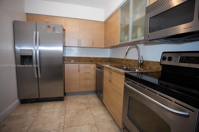 kitchen with sink, light brown cabinets, dark stone countertops, light tile patterned floors, and appliances with stainless steel finishes