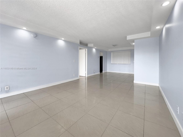 empty room with a textured ceiling and light tile patterned floors