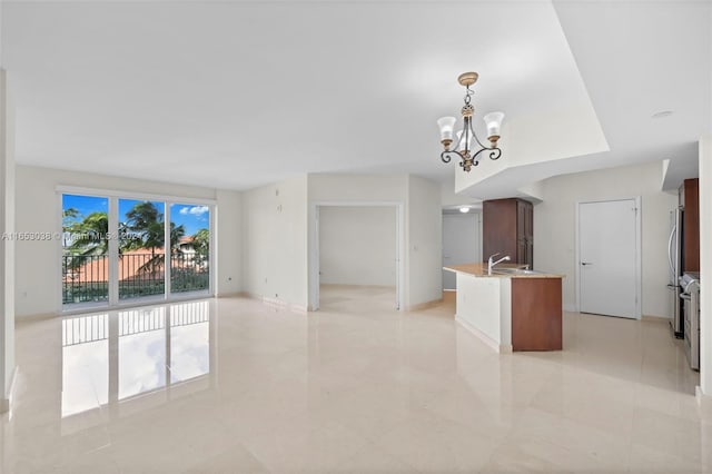 kitchen featuring pendant lighting, open floor plan, a sink, a chandelier, and baseboards