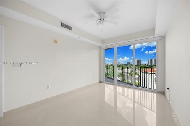 unfurnished room featuring ceiling fan, light tile patterned flooring, visible vents, baseboards, and a view of city