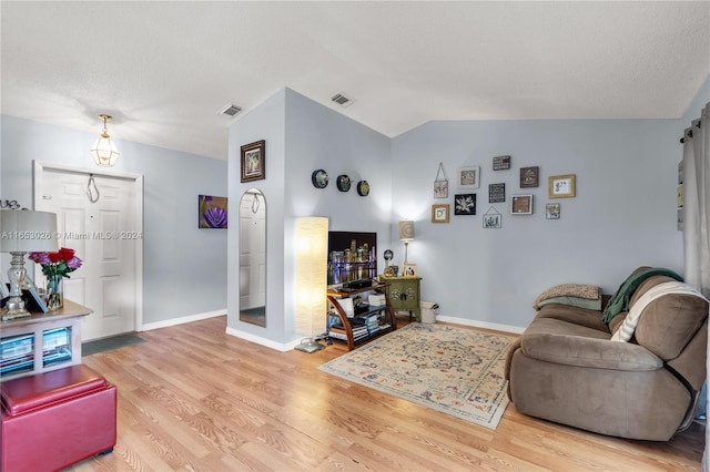 living room with vaulted ceiling, a textured ceiling, and light hardwood / wood-style floors