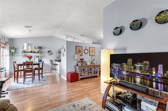 living room featuring vaulted ceiling, a textured ceiling, track lighting, and light hardwood / wood-style floors