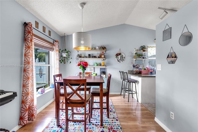 dining area with lofted ceiling, light hardwood / wood-style flooring, rail lighting, and a textured ceiling