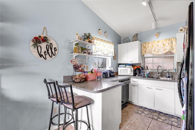 kitchen featuring a kitchen bar, black appliances, sink, lofted ceiling, and white cabinets