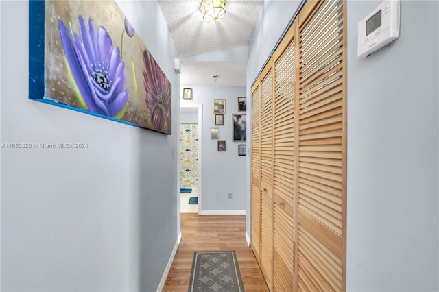 corridor with a textured ceiling, vaulted ceiling, and hardwood / wood-style flooring