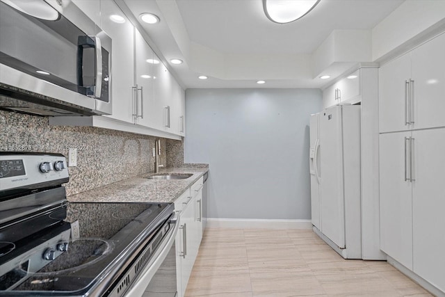 kitchen with backsplash, appliances with stainless steel finishes, sink, white cabinetry, and light stone counters