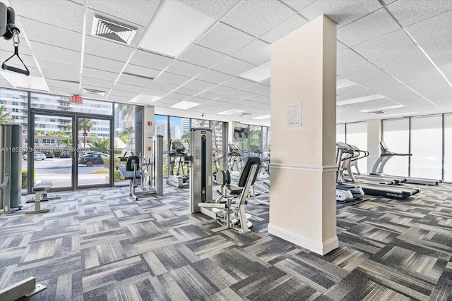 gym with dark carpet, a wall of windows, and a drop ceiling