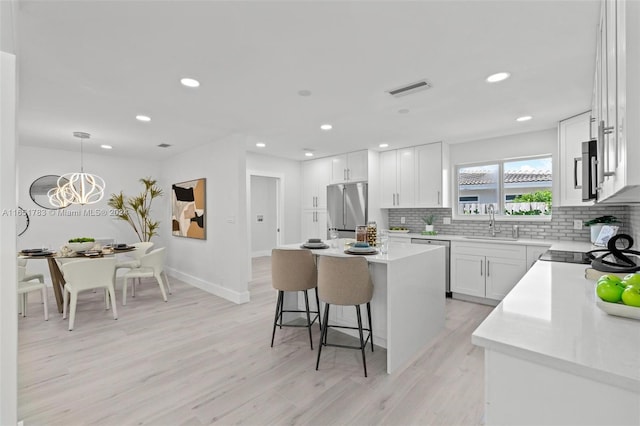 kitchen with white cabinetry, appliances with stainless steel finishes, decorative light fixtures, a kitchen island, and light wood-type flooring