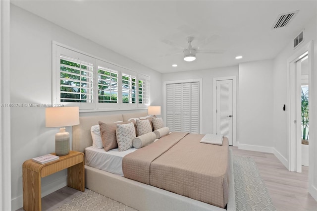 bedroom featuring multiple closets, ceiling fan, and light hardwood / wood-style flooring