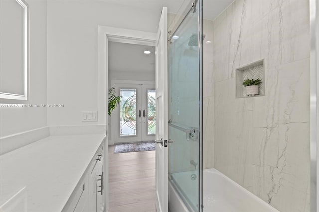 bathroom featuring hardwood / wood-style floors, french doors, vanity, and enclosed tub / shower combo