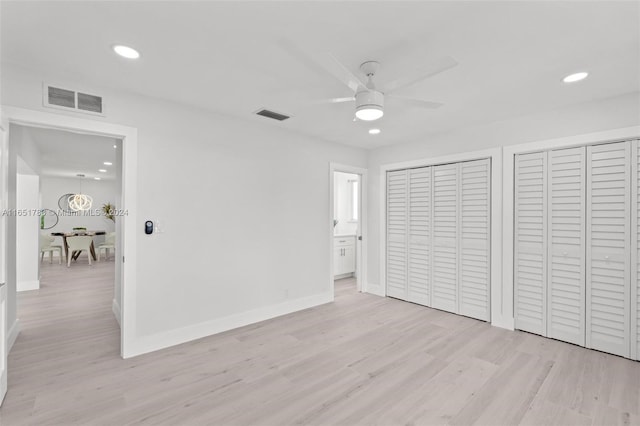 unfurnished bedroom featuring ceiling fan, light hardwood / wood-style floors, ensuite bath, and two closets