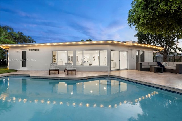 pool at dusk with outdoor lounge area and a patio area