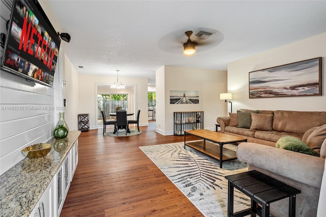 living room with ceiling fan with notable chandelier and dark hardwood / wood-style flooring