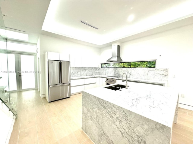 kitchen featuring wall chimney exhaust hood, high quality fridge, light hardwood / wood-style flooring, sink, and white cabinets