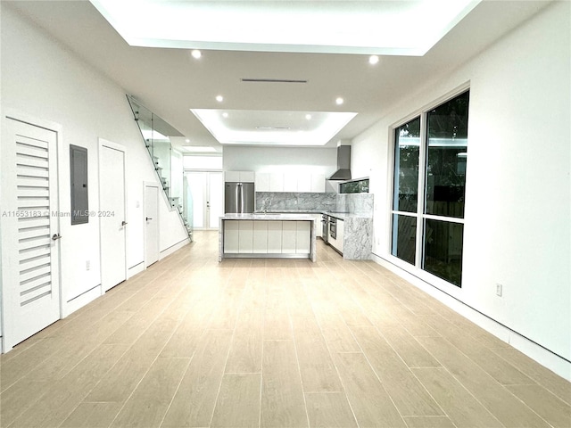 kitchen featuring a raised ceiling, white cabinets, wall chimney exhaust hood, light hardwood / wood-style floors, and appliances with stainless steel finishes