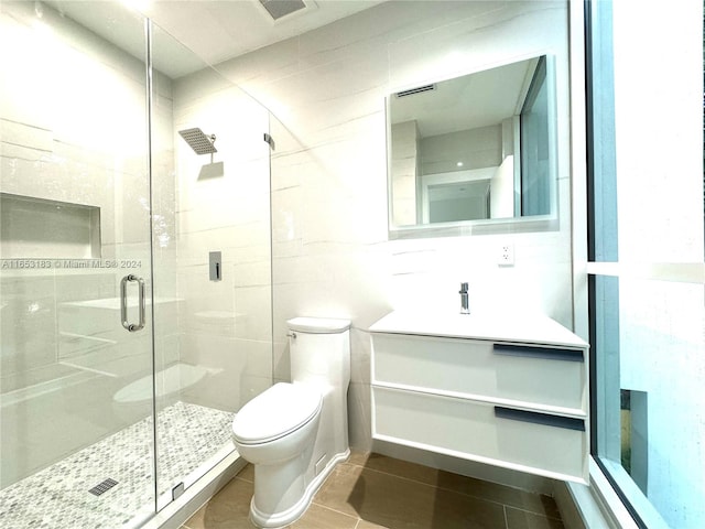 bathroom with walk in shower, toilet, tile patterned floors, tile walls, and vanity